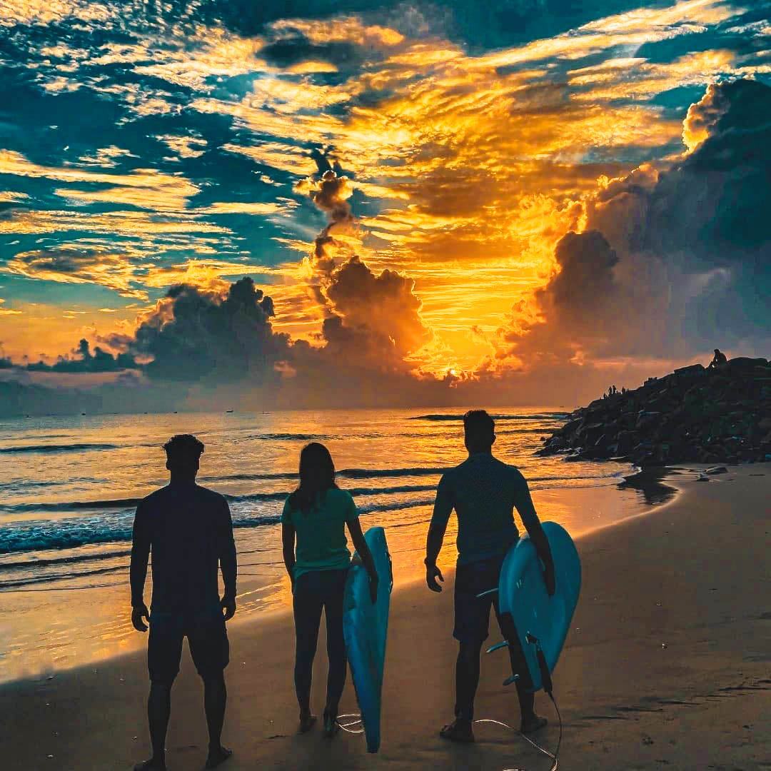 Surfers carrying their boards under an orange sunset sky